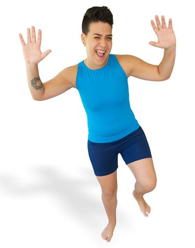 Outplay model wearing Outplay blue Flatsea full compression swim top paired with navy Boi shorts. Model is joyfully hoping on one foot and raising their hand